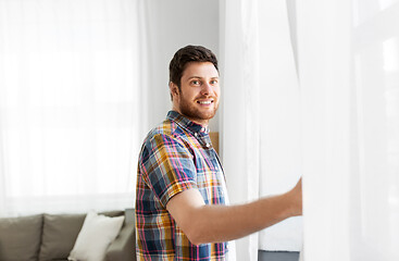 Image showing young man opening window curtain at home