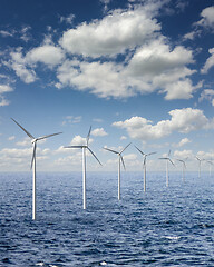 Image showing Row from wind turbines in an open sea water on a background of cloudy sky.