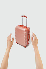 Image showing Woman hands try to take travel suitcase on a light grey background.