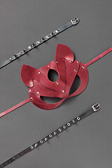 Image showing Red leather cat BDSM mask and stud collars on a black background.