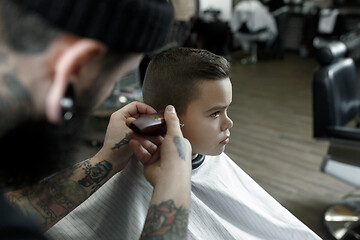 Image showing Children hairdresser cutting little boy against a dark background.