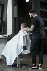 Image showing Children hairdresser cutting little boy against a dark background.