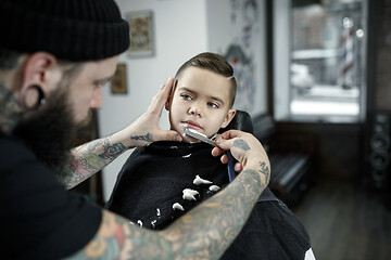 Image showing Children hairdresser cutting little boy against a dark background.