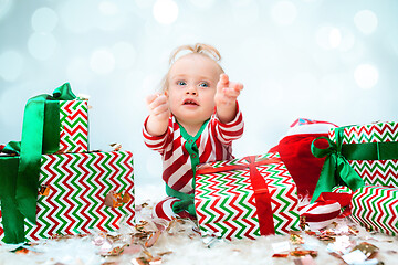 Image showing Cute baby girl 1 year old near santa hat posing over Christmas background. Sitting on floor with Christmas ball. Holiday season.