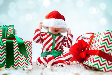 Image showing Cute baby girl 1 year old wearing santa hat posing over Christmas background. Sitting on floor with Christmas ball. Holiday season.