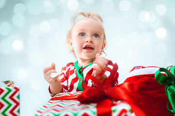 Image showing Cute baby girl 1 year old near santa hat posing over Christmas background. Sitting on floor with Christmas ball. Holiday season.