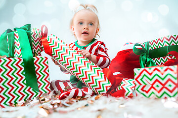 Image showing Cute baby girl 1 year old near santa hat posing over Christmas background. Sitting on floor with Christmas ball. Holiday season.