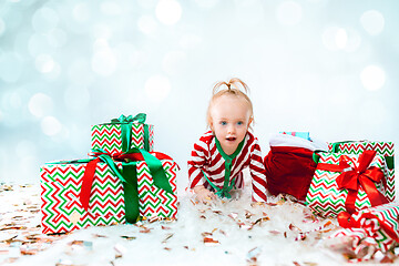 Image showing Cute baby girl 1 year old near santa hat posing over Christmas background. Sitting on floor with Christmas ball. Holiday season.