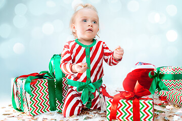 Image showing Cute baby girl 1 year old near santa hat posing over Christmas background. Sitting on floor with Christmas ball. Holiday season.