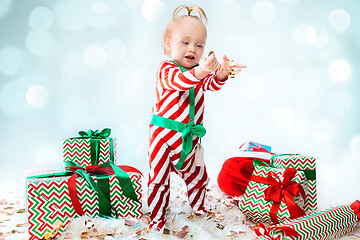 Image showing Cute baby girl 1 year old wearing santa hat posing over Christmas background. Sitting on floor with Christmas ball. Holiday season.