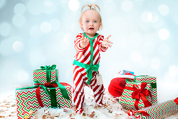 Image showing Cute baby girl 1 year old wearing santa hat posing over Christmas background. Sitting on floor with Christmas ball. Holiday season.