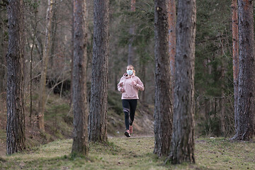 Image showing Corona virus, or Covid-19, is spreading all over the world. Portrait of caucasian sporty woman wearing a medical protection face mask while running in nature.