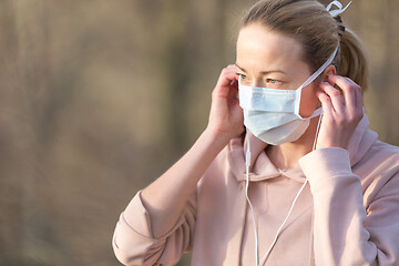 Image showing Portrait of caucasian sporty woman wearing medical protection face mask while walking in park, relaxing and listening to music. Corona virus, or Covid-19, is spreading all over the world