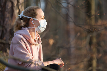 Image showing Portrait of caucasian sporty woman wearing medical protection face mask while relaxing in nature and listening to music. Corona virus, or Covid-19, is spreading all over the world