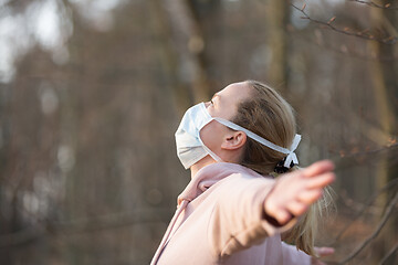 Image showing Portrait of caucasian sporty woman wearing medical protection face mask while relaxing by taking a deep breath in forest. Corona virus, or Covid-19, is spreading all over the world