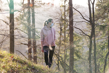 Image showing Corona virus, or Covid-19, is spreading all over the world. Portrait of caucasian sporty woman wearing a medical protection face mask while walking in the forest. Corona virus.