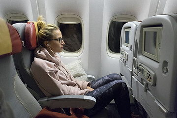 Image showing Sporty casual young blonde caucasian lady watching movie while traveling by airplane by the window. Commercial transportation by planes