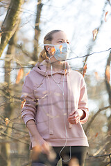 Image showing Portrait of caucasian sporty woman wearing medical protection face mask while walking in park, relaxing and listening to music. Corona virus, or Covid-19, is spreading all over the world