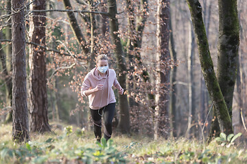 Image showing Corona virus, or Covid-19, is spreading all over the world. Portrait of caucasian sporty woman wearing a medical protection face mask while running in nature.