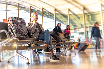 Image showing Casual blond young woman using her cell phone while waiting to board a plane at bussy airport departure gates.