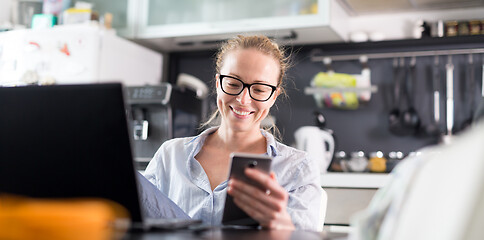 Image showing Stay at home and social distancing. Woman in her casual home clothing working remotly from her kitchen dining table in the morning. Video chatting with friend, family or business clients or partners