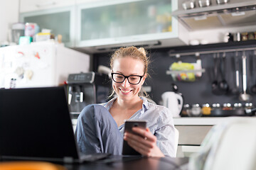 Image showing Stay at home and social distancing. Woman in her casual home clothing working remotly from her kitchen dining table in the morning. Video chatting with friend, family or business clients or partners