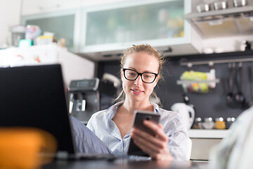 Image showing Stay at home and social distancing. Woman in her casual home clothing working remotly from her kitchen dining table in the morning. Video chatting with friend, family or business clients or partners