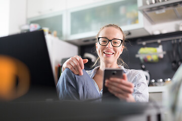 Image showing Stay at home and social distancing. Woman in her casual home clothing working remotly from kitchen dining table. Video chatting using social media with friend, family, business clients or partners