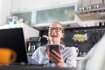 Image showing Stay at home and social distancing. Woman in her casual home clothing working remotly from kitchen dining table. Video chatting using social media with friend, family, business clients or partners