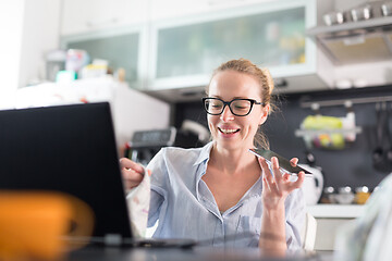 Image showing Stay at home and social distancing. Woman in her casual home clothing working remotly from kitchen dining table. Video chatting using social media with friend, family, business clients or partners