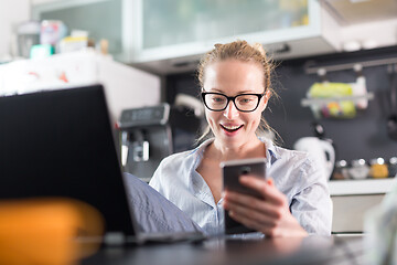 Image showing Stay at home and social distancing. Woman in her casual home clothing working remotly from kitchen dining table. Video chatting using social media with friend, family, business clients or partners