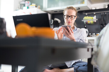 Image showing Stay at home and social distancing. Woman in her casual home clothing working remotly from kitchen dining table. Video chatting using social media with friend, family, business clients or partners