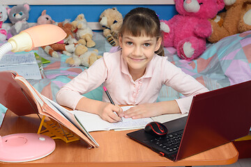 Image showing A child learns at home at a desk with toys in the background