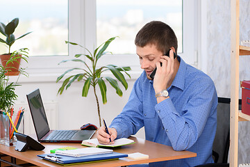 Image showing Office employee with a smile talking on the phone and writes in a diary