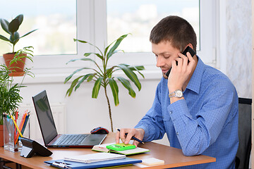 Image showing An office employee is smiling on the phone and counting on a calculator