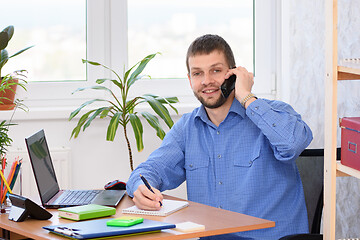 Image showing An office employee is talking on the phone with a smile and looked in frame