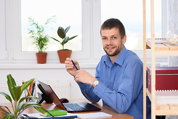 Image showing Business office worker sits at a table in the office and holds a pen in his hands