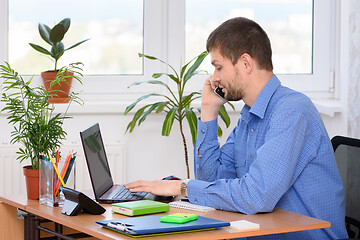 Image showing The specialist in the office works at the computer and talks on the phone