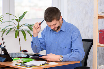 Image showing Office employee reads a document, smiles and scratches his head with a pen