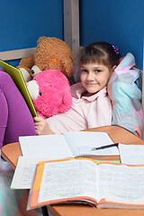 Image showing The girl looks into the frame with a smile holding a tablet, in front of her lie textbooks and notebooks