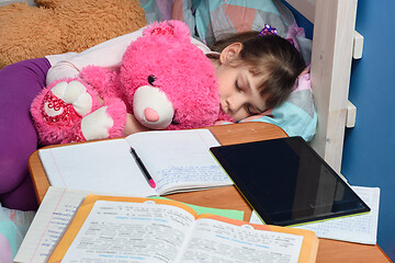 Image showing Girl sleeps with a teddy bear near a desk with textbooks and a tablet