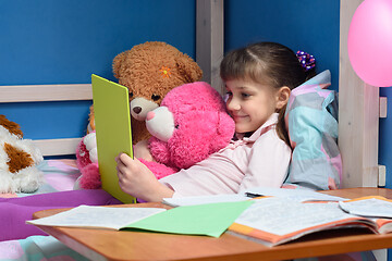 Image showing Nine-year-old girl lies on bed with toys and looks at tablet