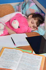 Image showing Girl fell asleep in a hug with a teddy bear doing lessons at home