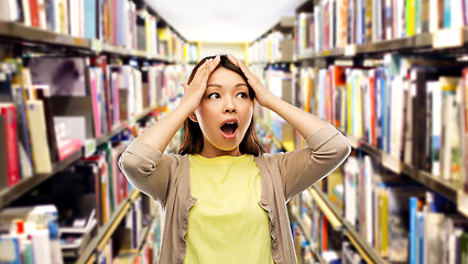 Image showing stressed asian woman holding to head at library