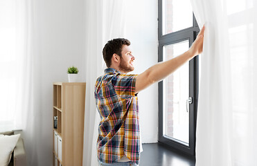 Image showing young man opening window curtain at home