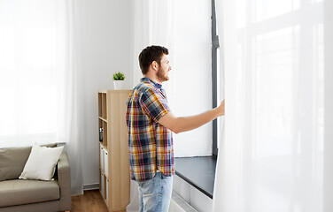 Image showing young man opening window curtain at home