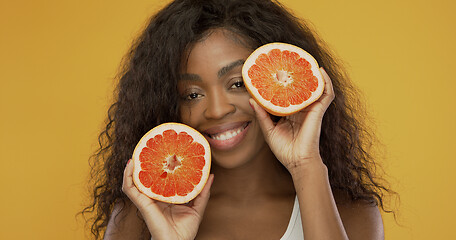 Image showing Cheerful black lady showing halves of grapefruit