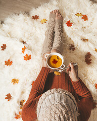 Image showing Woman holds a bowl of spiced pumpkin soup sitting on cozy rug