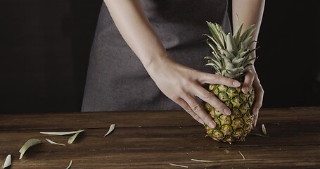 Image showing Woman\' hands with ripe juicy natural organic tropical fruit pineapple on a wooden kitchen table on a black background.