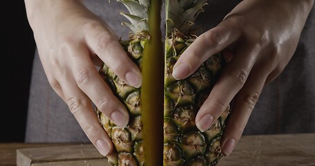 Image showing Close up view. Woman\'s hands hold two pieces of juicy fresh natural organic pineapple on a wooden background.